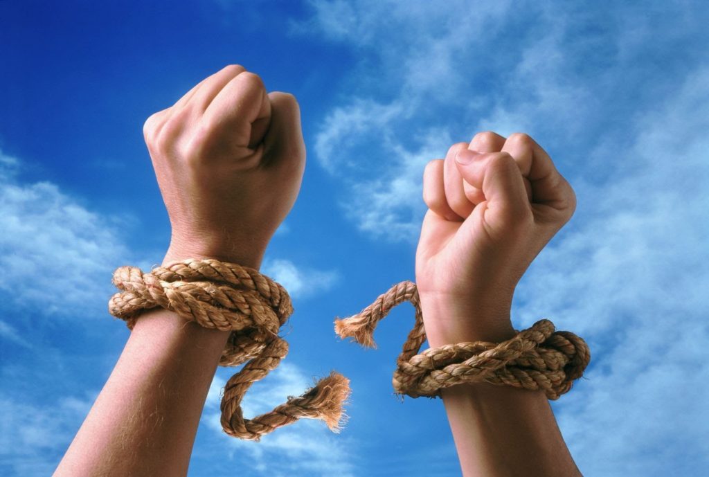 a pair of hands breaking free from a rope tied around their wrists with the blue sky in the background
